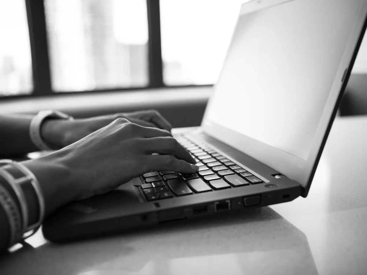 Gros plan en noir et blanc de mains tapant sur le clavier d'un ordinateur portable