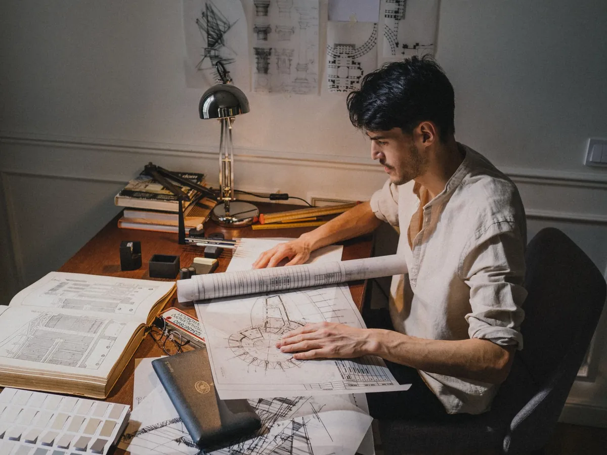 Jeune architecte travaillant sur des plans à son bureau, éclairé par une lampe