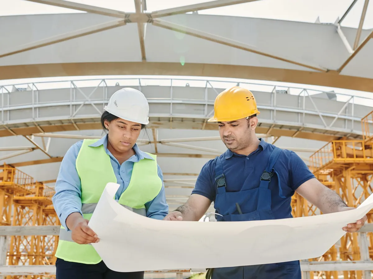 Ingénieurs hommes et femmes échangeant sur des plans sur un chantier de construction
