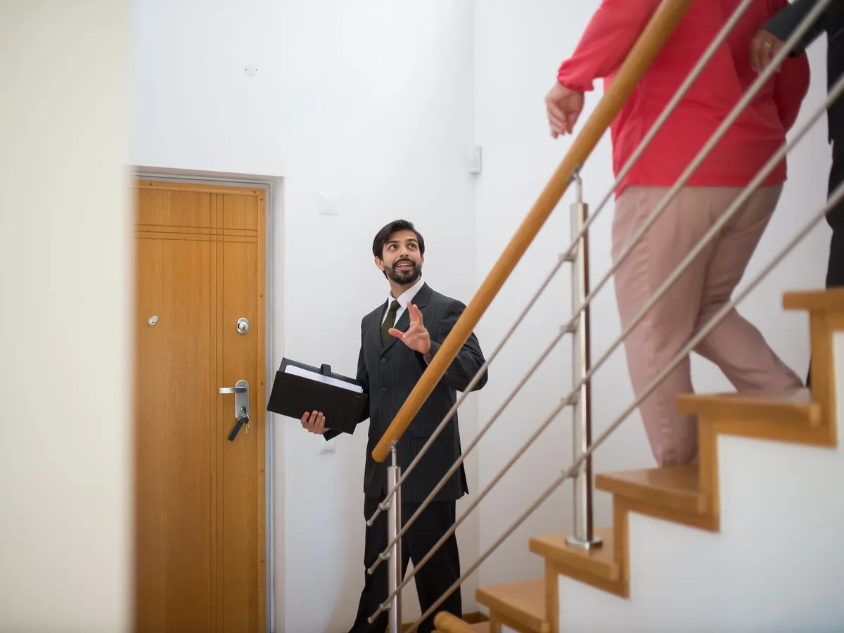 Agent immobilier faisant visiter une maison moderne à des acheteurs potentiels, dans l'escalier