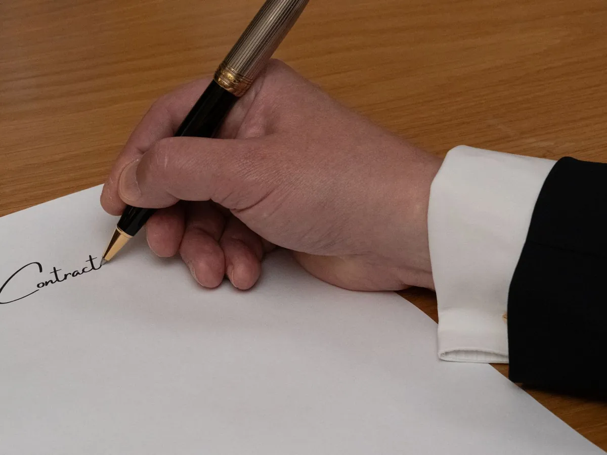 Professionnel signant un contrat d'affaires avec un stylo plume sur un bureau en bois