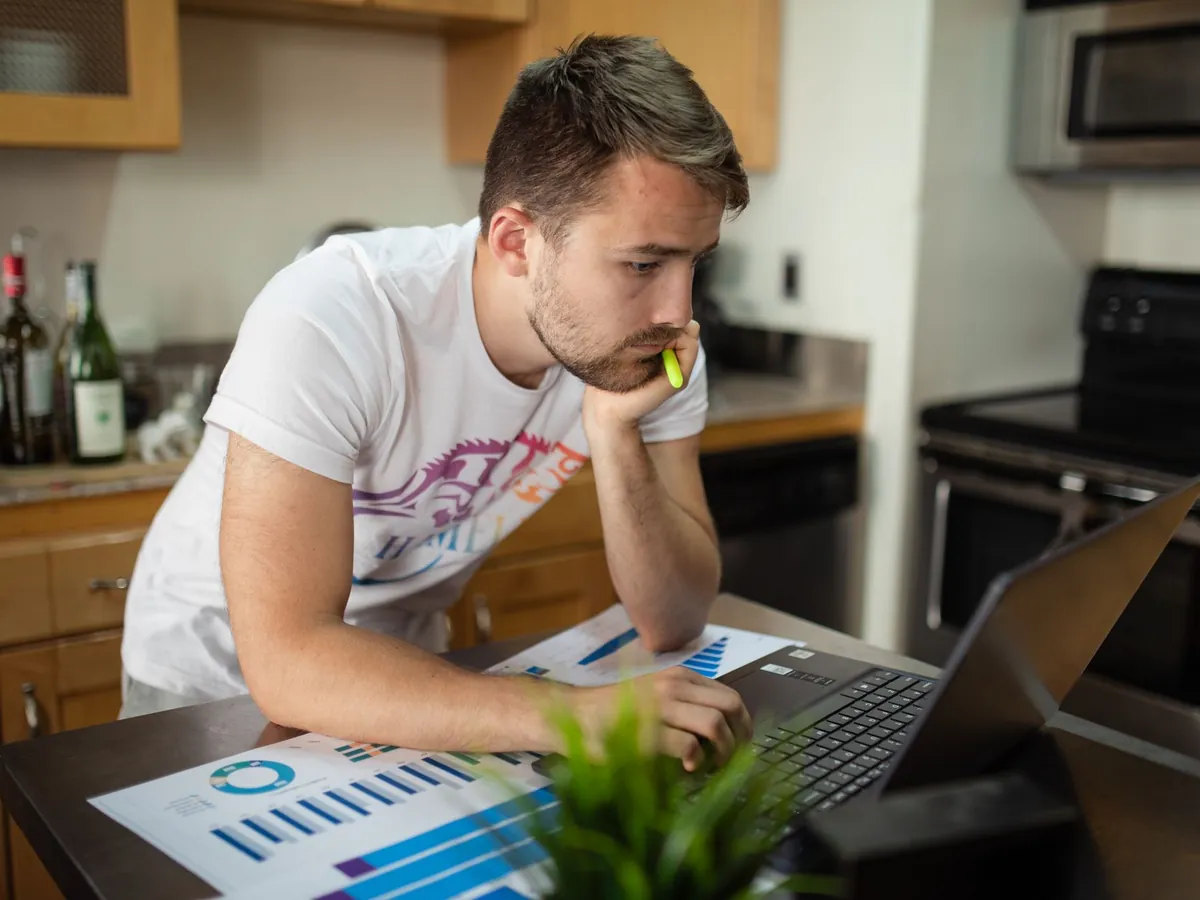 Jeune homme concentré sur l'analyse de données à domicile, ordinateur portable et graphiques