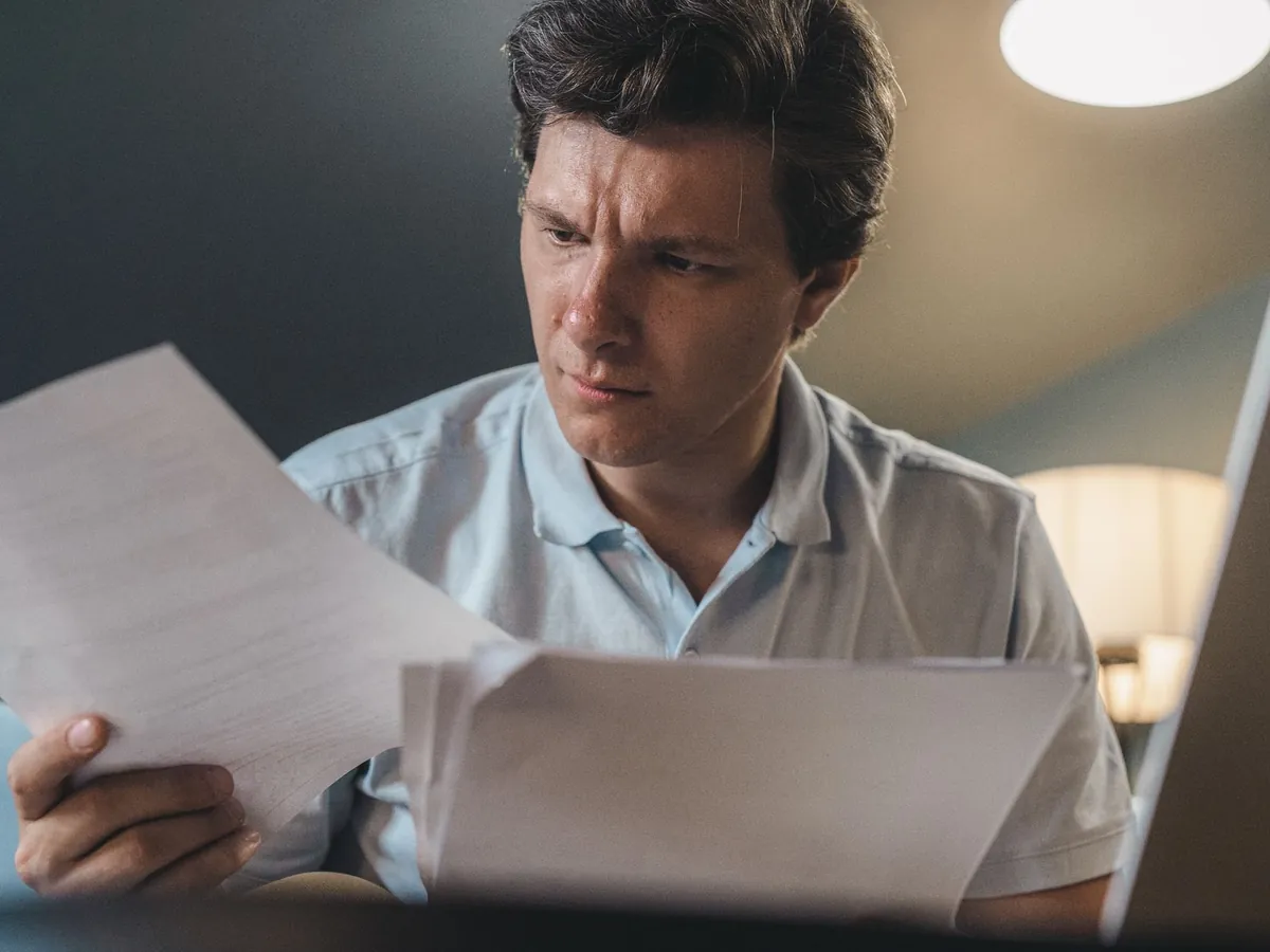 Homme absorbé par l'examen de documents, assis à l'intérieur sous un éclairage chaleureux