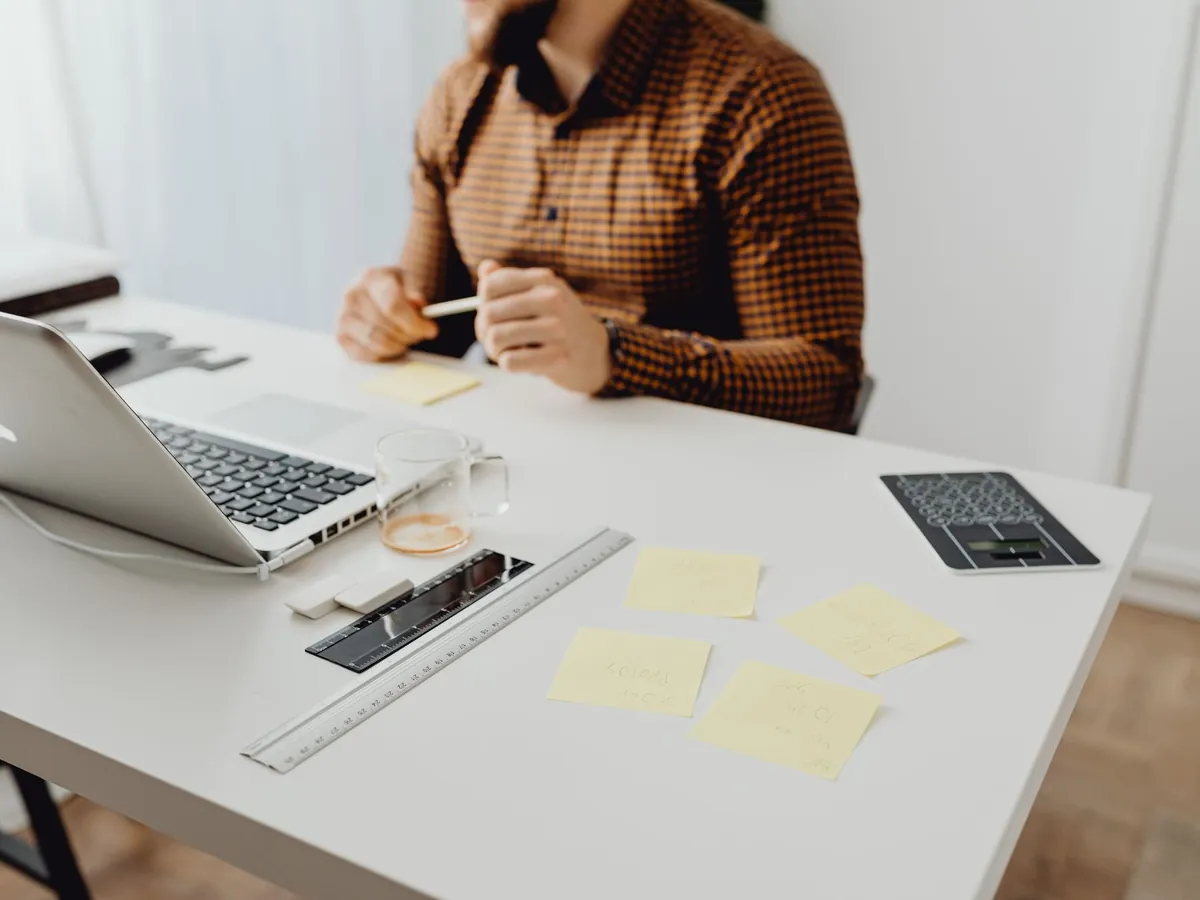 Espace de travail moderne avec ordinateur portable, fournitures et personne en chemise à carreaux