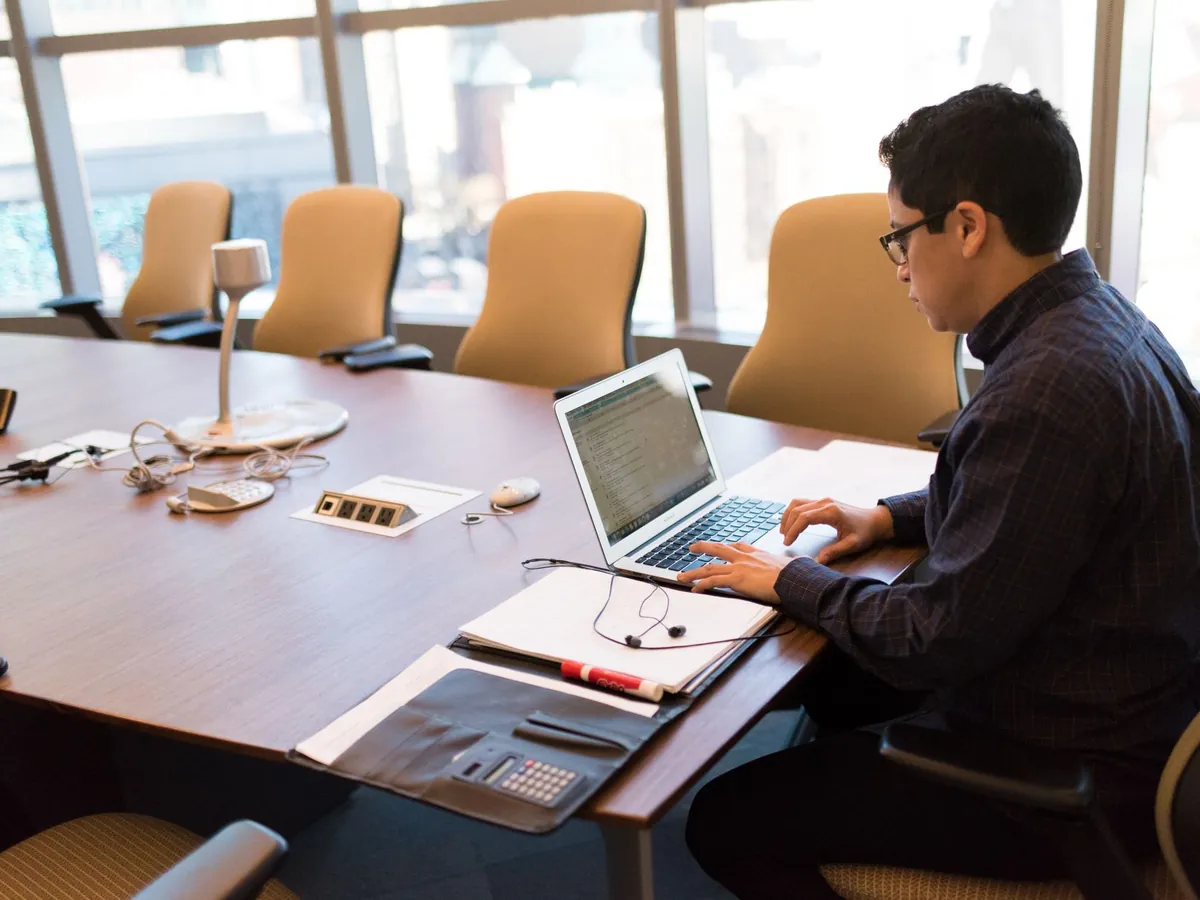 Professionnel assis à un bureau avec son ordinateur portable, dans une salle de réunion lumineuse