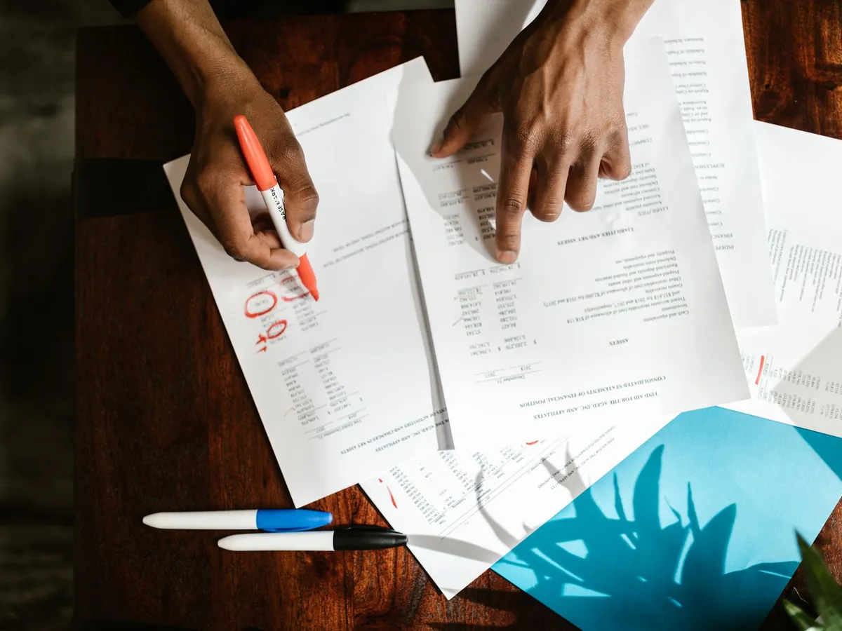 Vue de dessus de mains annotant des documents financiers posés sur un bureau