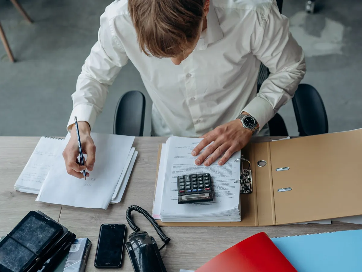 Homme dans un bureau examinant des documents financiers avec une calculatrice sur la table