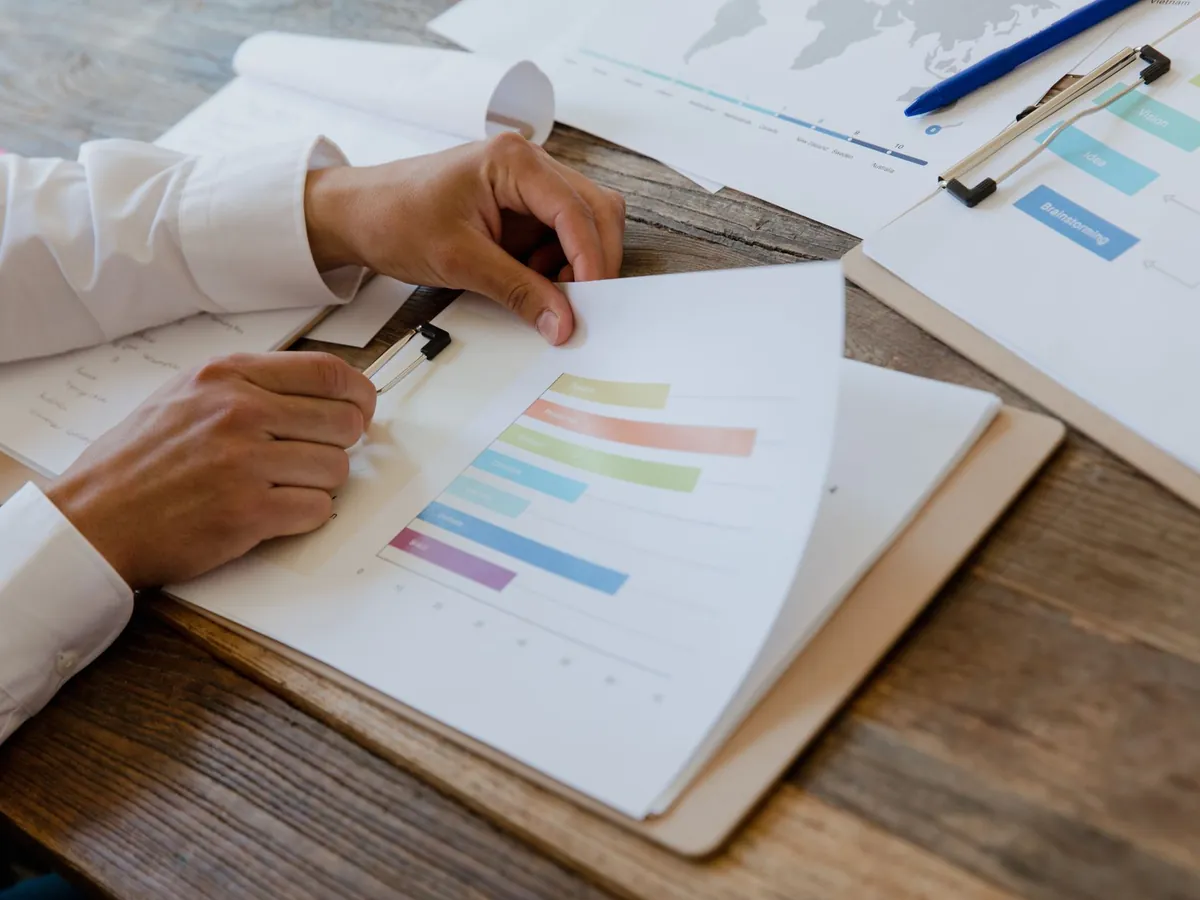 Gros plan de mains examinant un rapport d'activité illustré de graphiques colorés sur un bureau en bois
