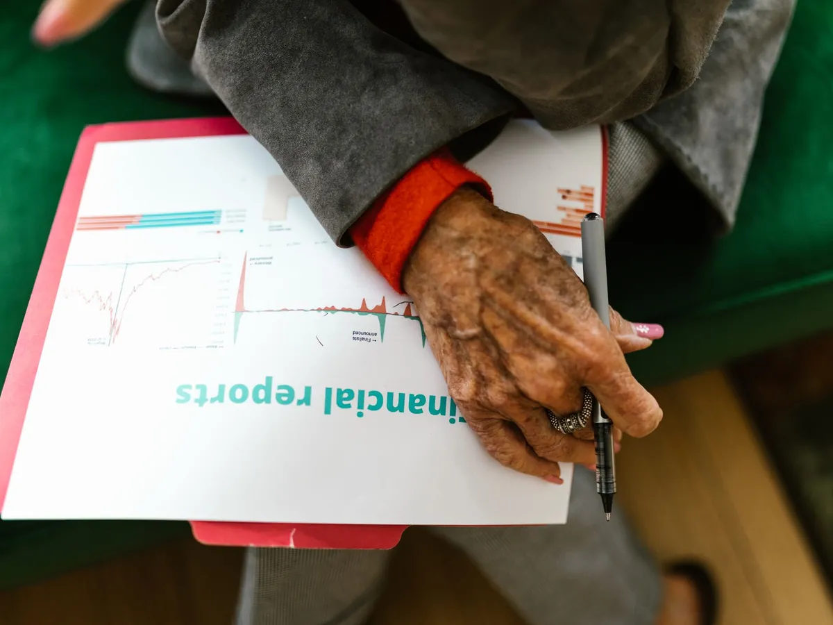 Gros plan d'une femme âgée tenant un stylo au-dessus d'un rapport financier