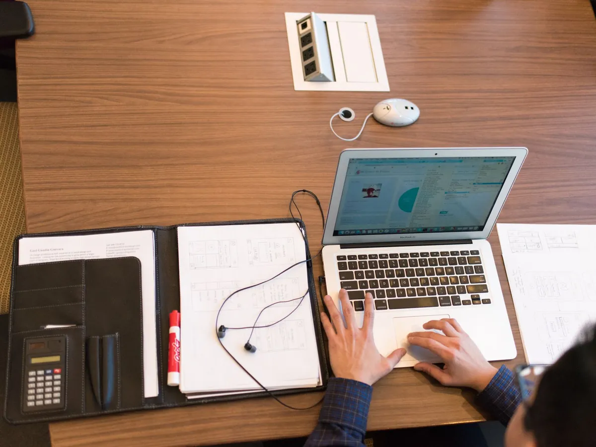 Vue de dessus d'une personne en télétravail, avec ordinateur portable et documents sur un bureau en bois