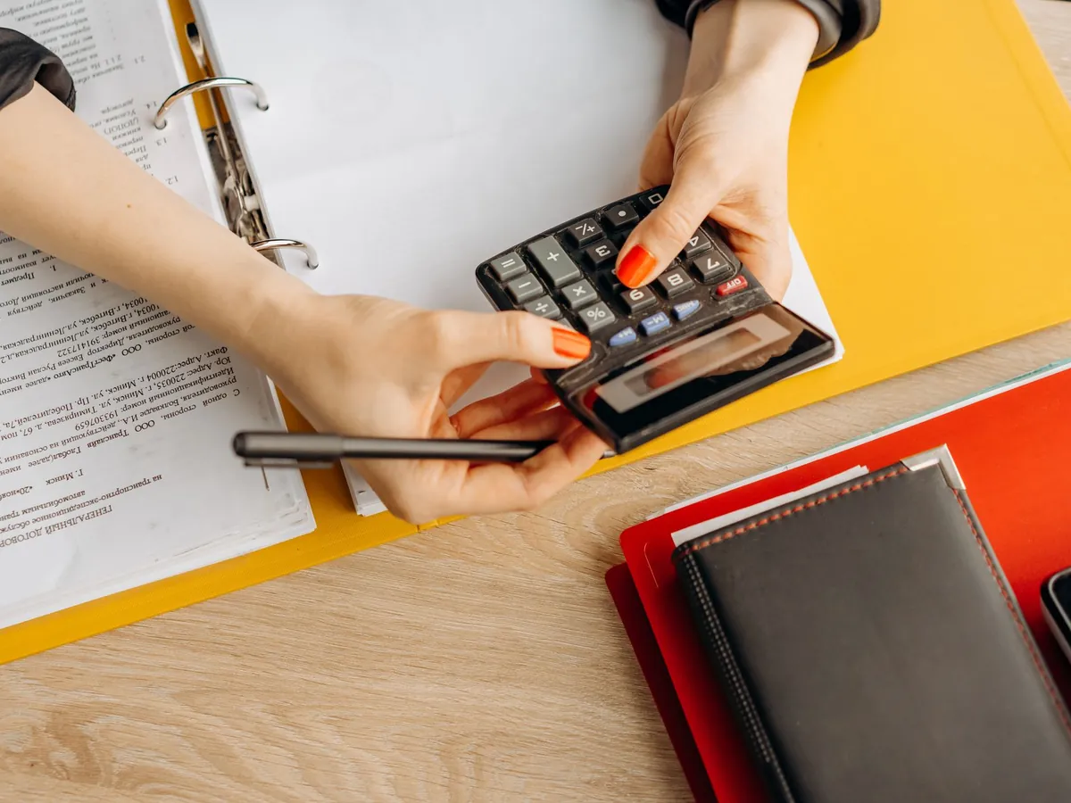 Mains utilisant une calculatrice sur un bureau, parmi documents et dossiers de comptabilité