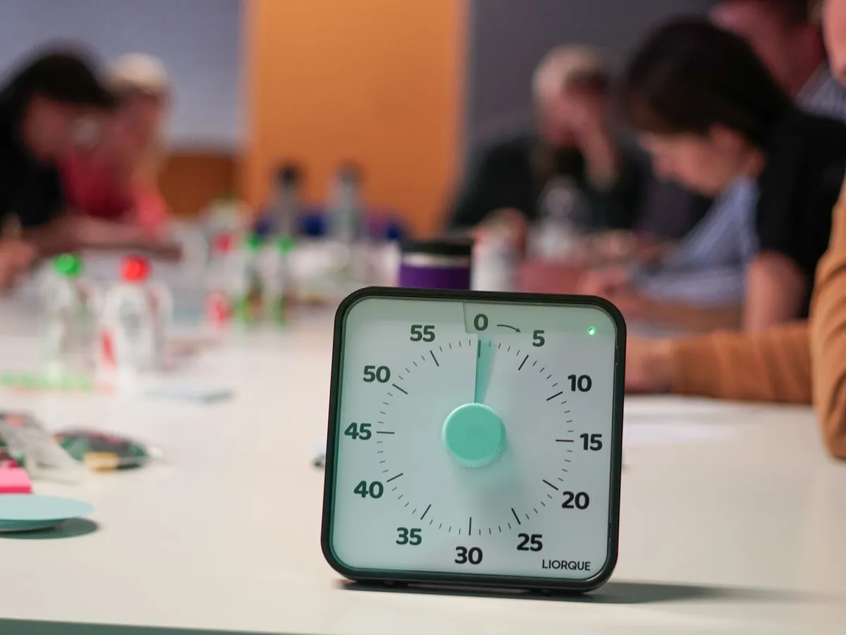 Minuteur posé sur une table, personnes floues en réunion de bureau, mettant l'accent sur la concentration