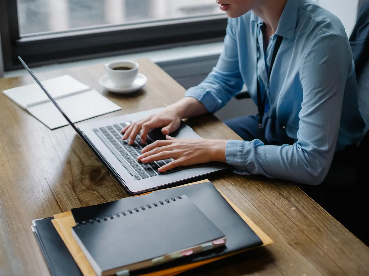 Employé tapant sur son ordinateur portable, café et carnets sur le bureau, dans un cadre concentré