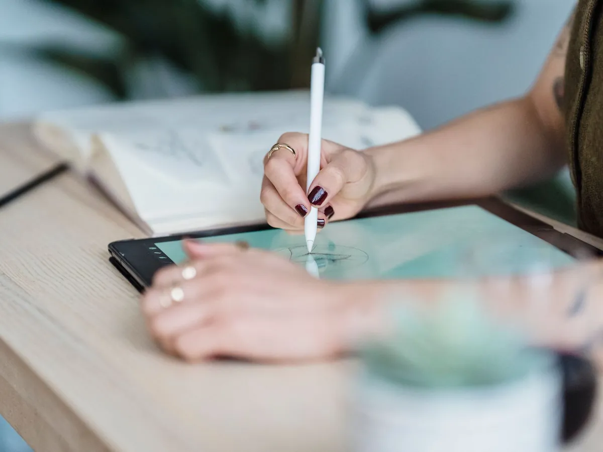 Gros plan sur une graphiste anonyme dessinant à la tablette et au stylet sur une table en bois