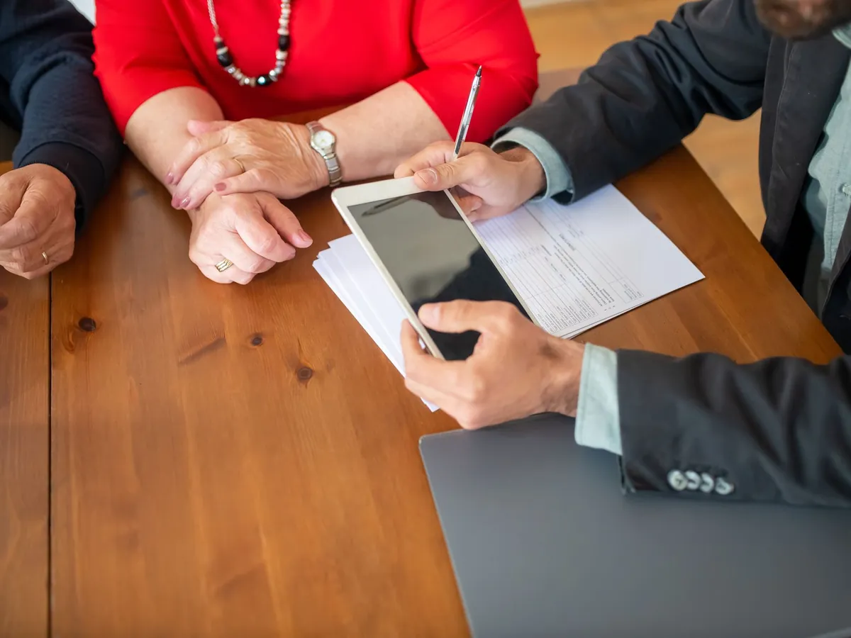Réunion d'affaires autour d'une table en bois, consultant examinant des documents sur une tablette