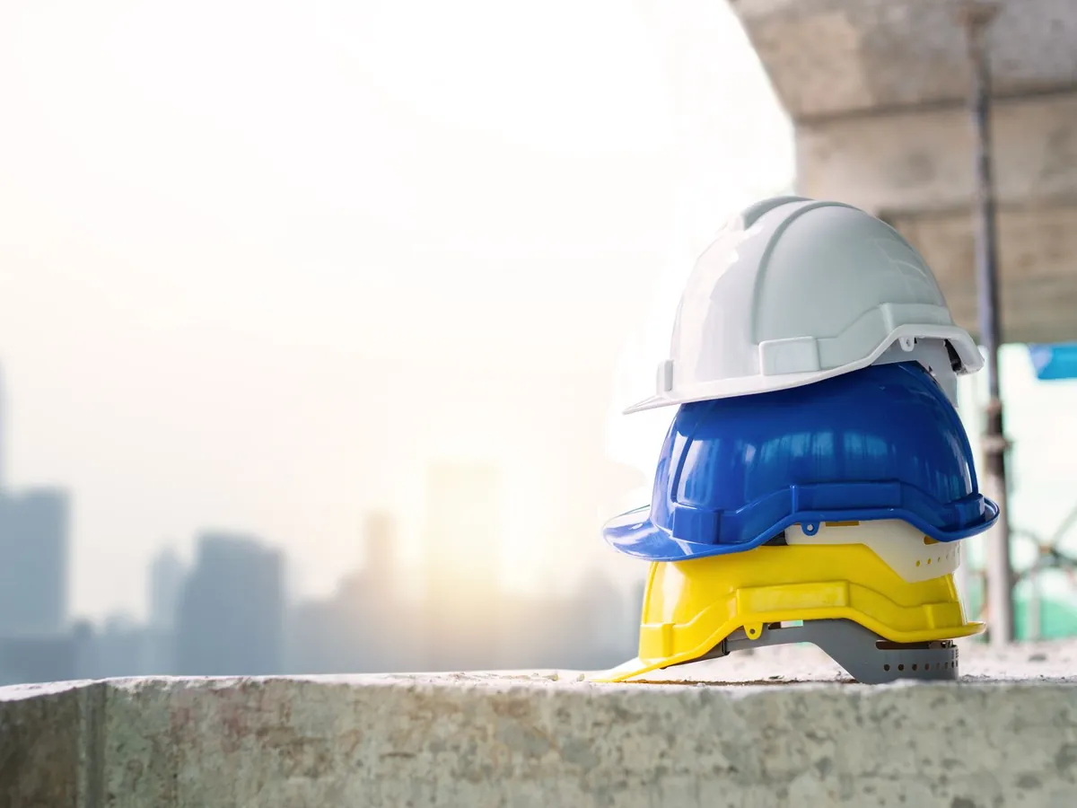 Trois casques de sécurité colorés empilés sur du béton, avec la skyline de la ville en arrière-plan