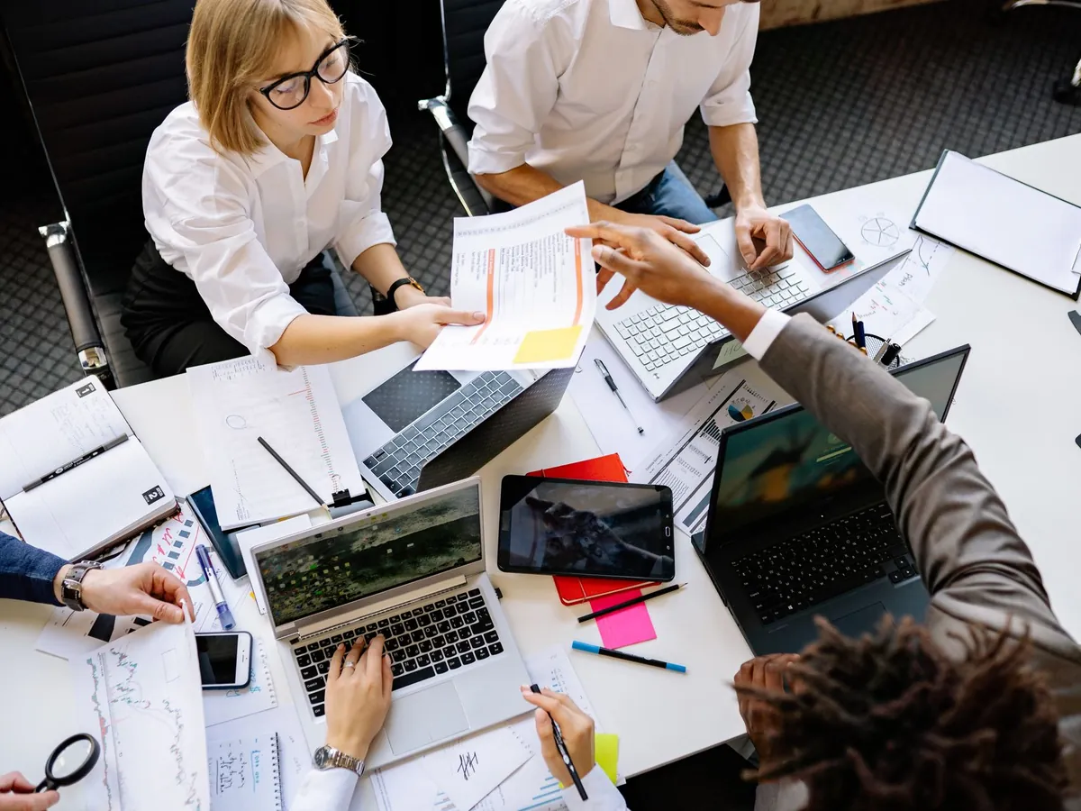 Équipe mixte en collaboration dans un bureau moderne, ordinateurs portables et documents sur la table