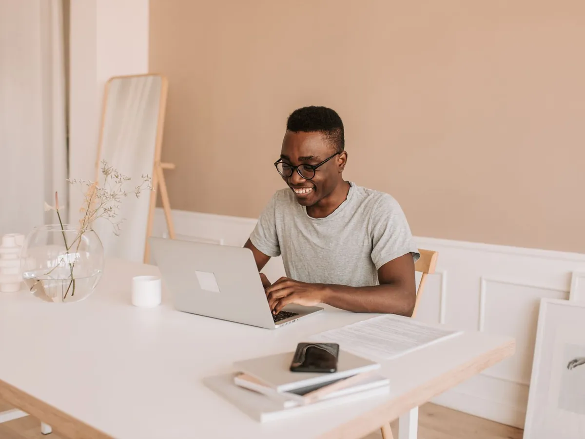 Jeune homme souriant tapant sur son ordinateur portable dans un bureau à domicile lumineux