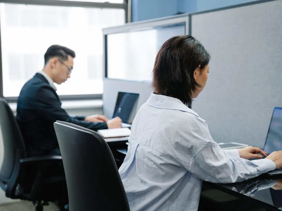 Deux professionnels travaillant sur leurs ordinateurs portables, dans des postes de bureau modernes