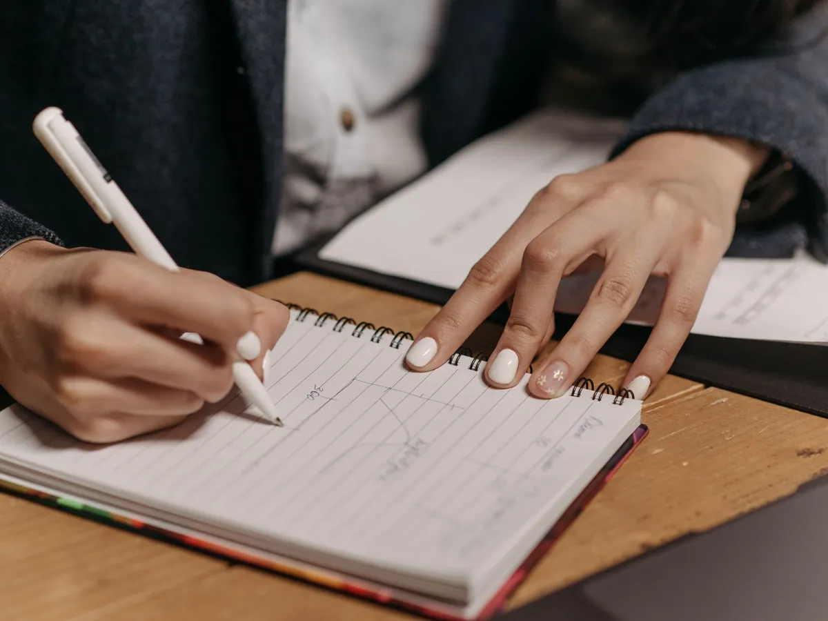 Gros plan d'une personne prenant des notes dans un cahier à spirale, sur un bureau en bois