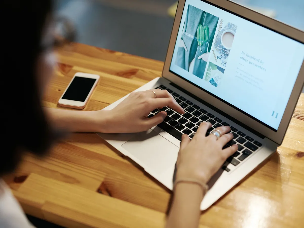 Personne tapant sur un ordinateur portable à une table en bois, smartphone à proximité, en télétravail