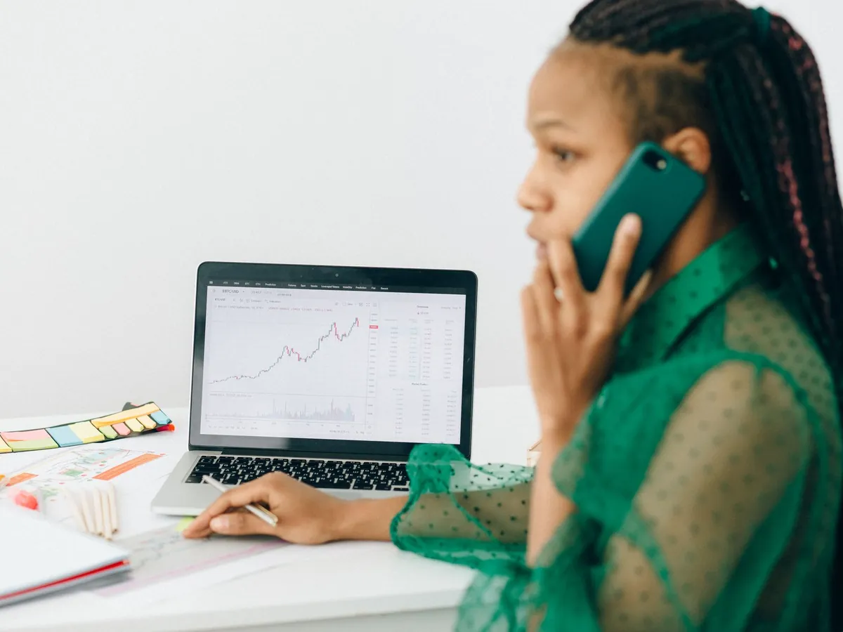 Femme afro-américaine examinant des graphiques boursiers sur un ordinateur portable tout en téléphonant