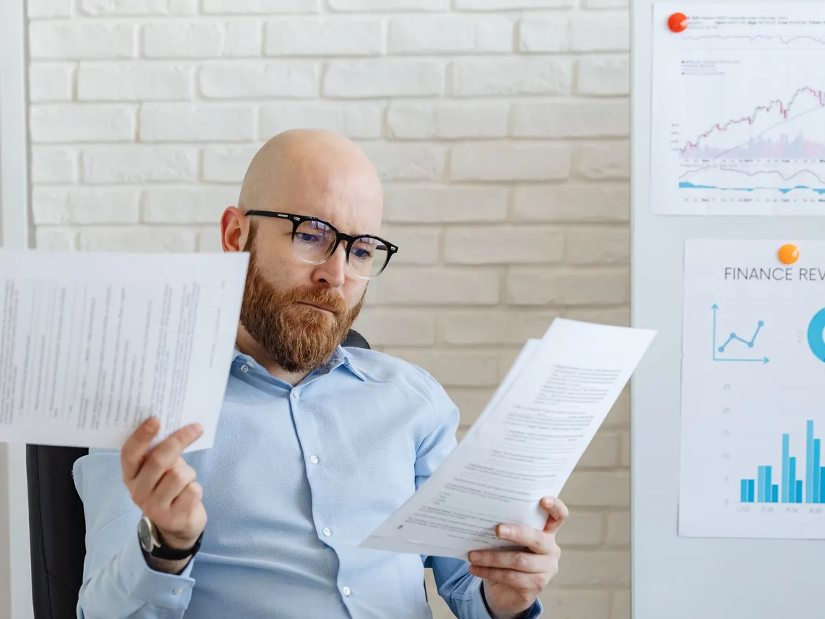 Homme d'affaires chauve et barbu lisant des documents financiers dans un bureau moderne