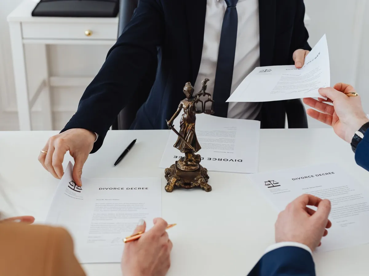 Trois adultes discutant de documents de divorce dans un bureau formel, statue de la Justice en vue