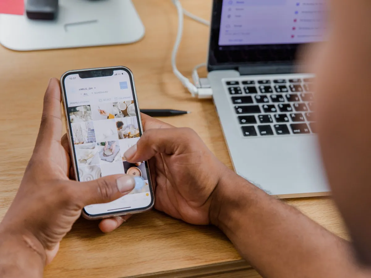 Gros plan d'une personne utilisant son smartphone et son ordinateur portable sur un bureau en bois
