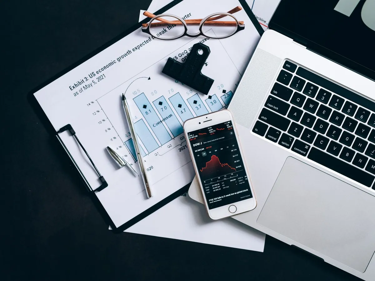 Vue de dessus de documents financiers, ordinateur portable et smartphone affichant des cours boursiers