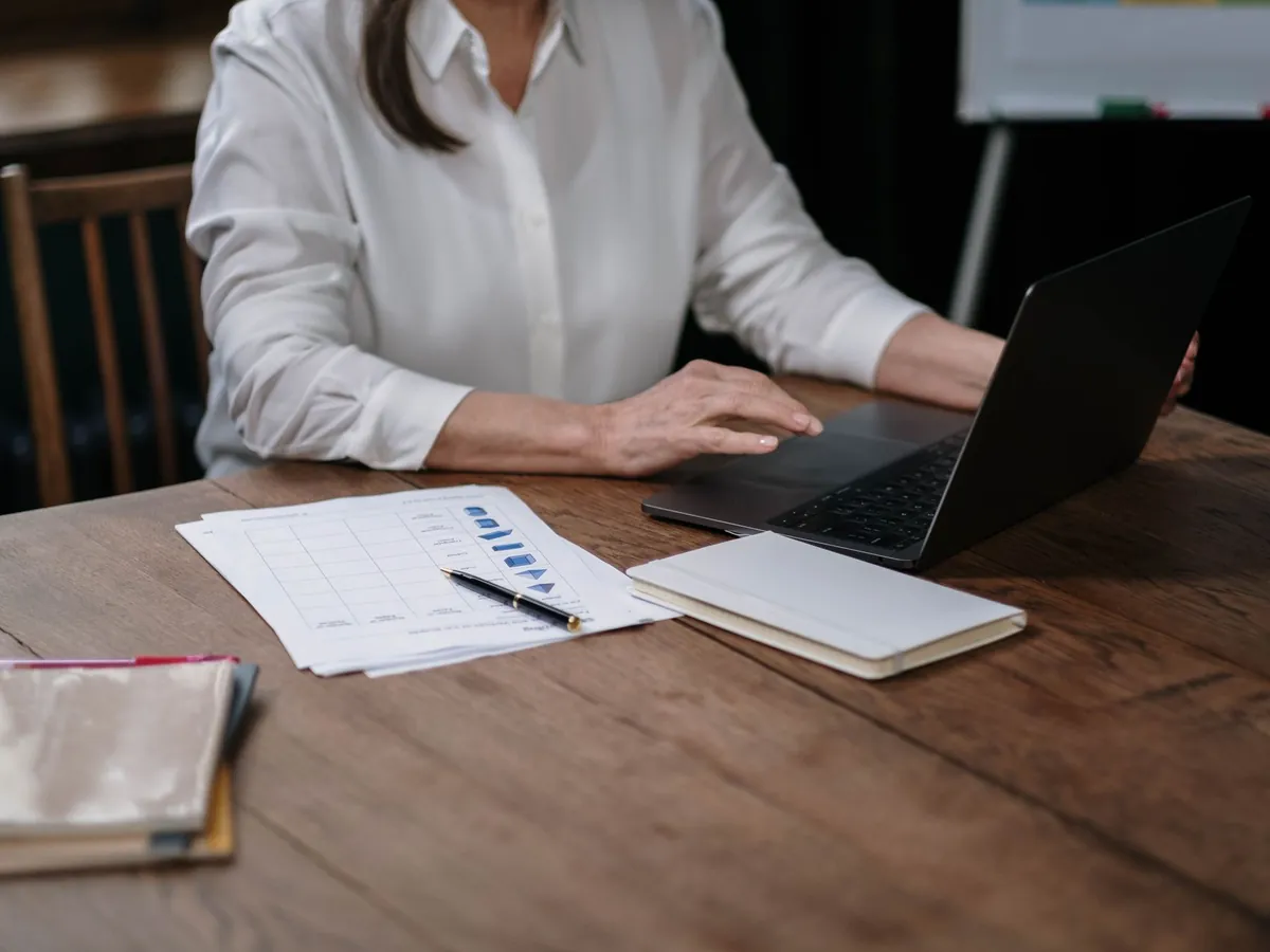 Femme d'affaires en chemise blanche travaillant sur son ordinateur portable, documents sur un bureau en bois