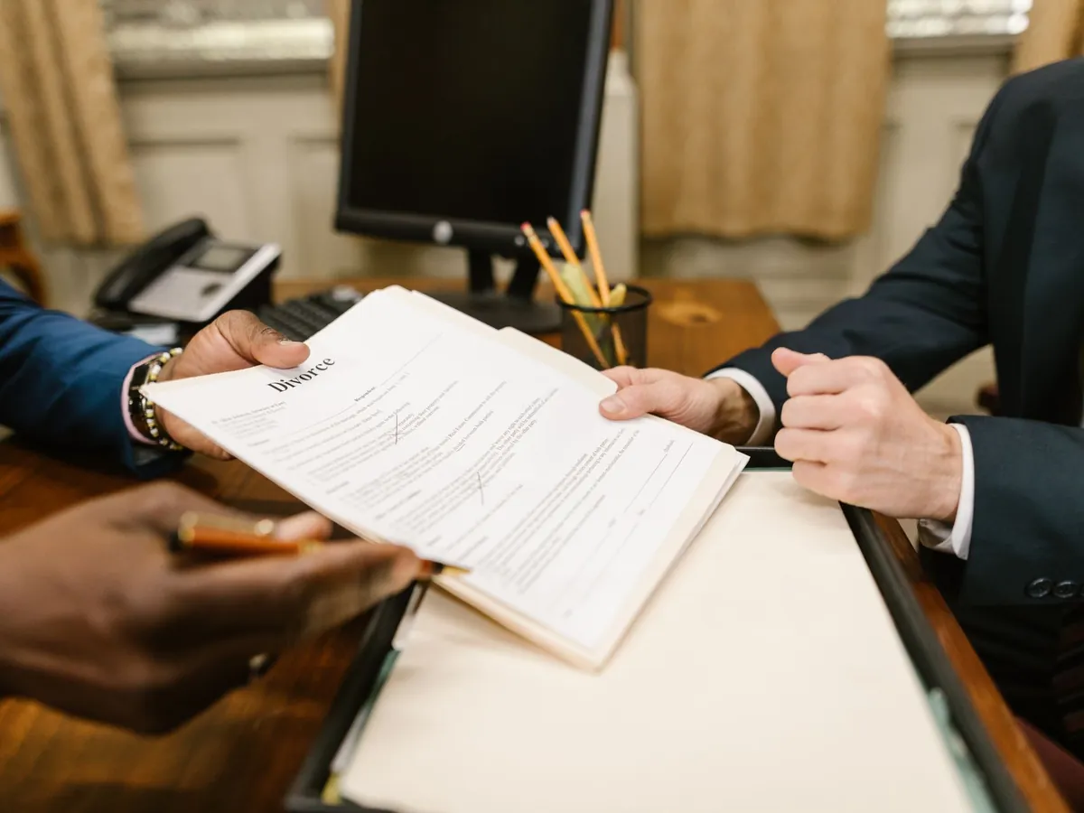 Gros plan de mains échangeant des documents de divorce pendant une procédure judiciaire au bureau