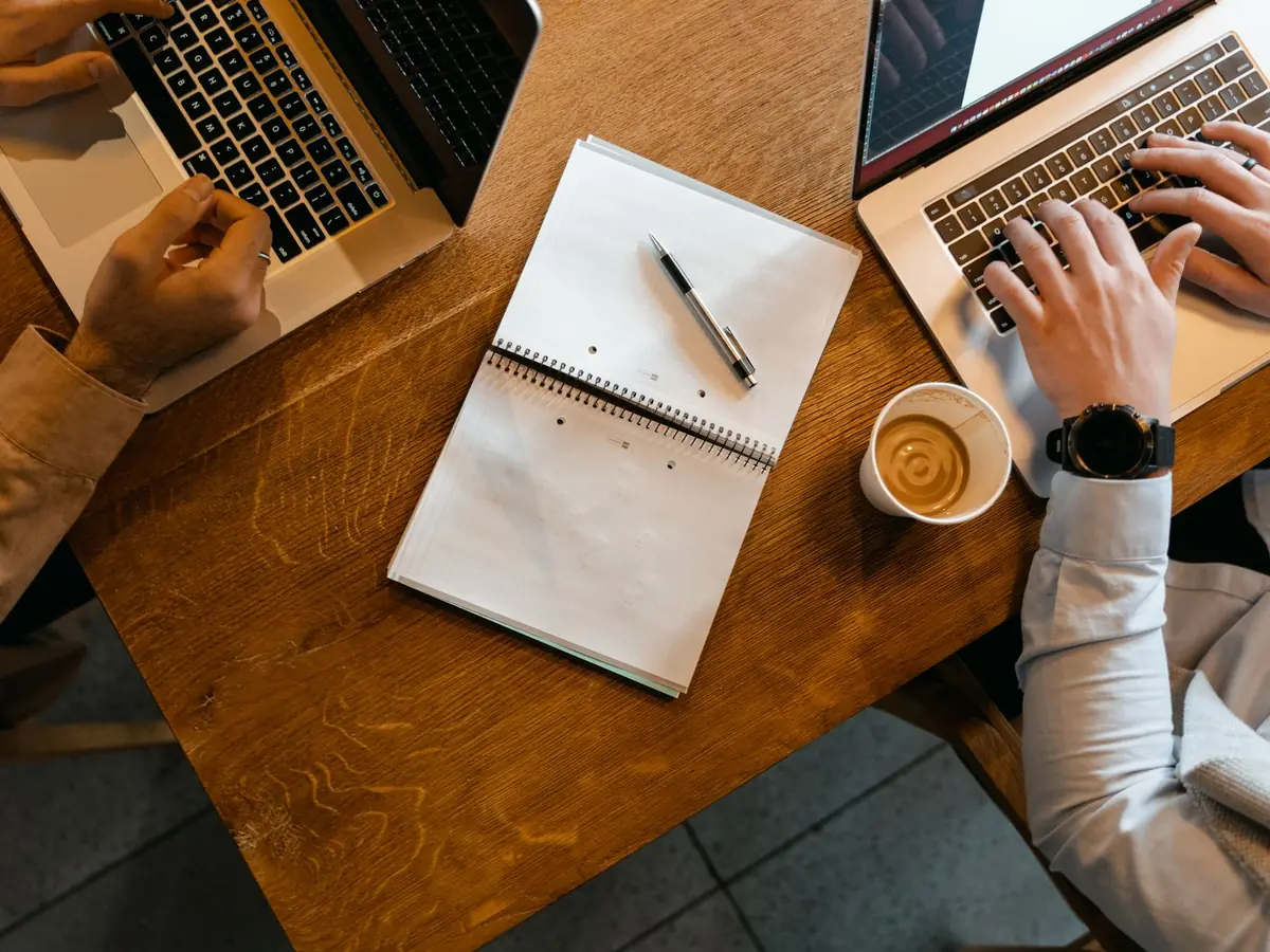 Vue de dessus de collègues travaillant sur ordinateurs portables, notes et café sur un bureau en bois