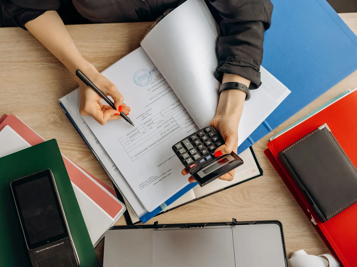 Comptable analysant des documents financiers à l'aide d'une calculatrice sur son bureau
