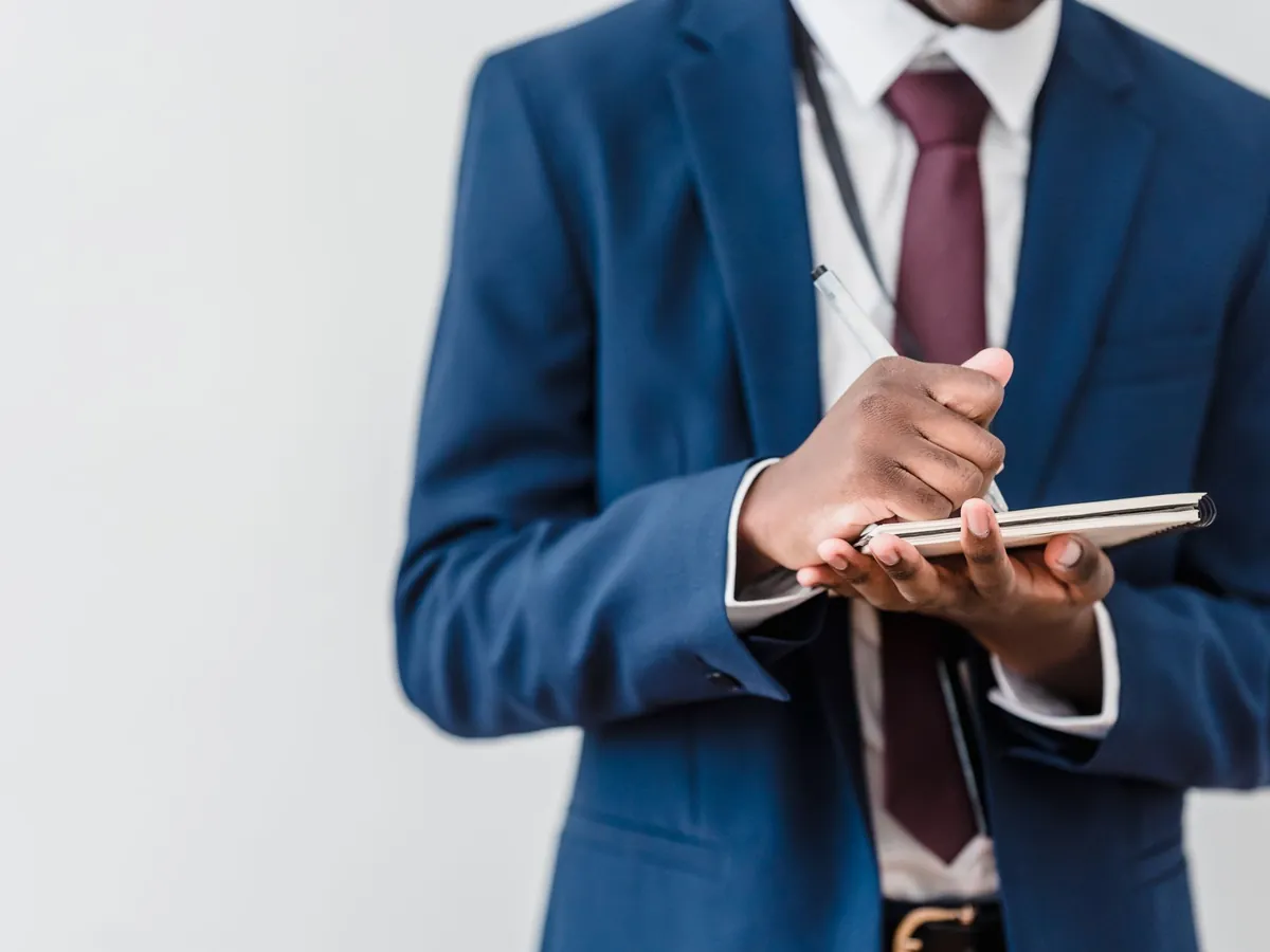 Gros plan d'un professionnel en costume bleu et cravate rouge, prenant des notes dans un carnet
