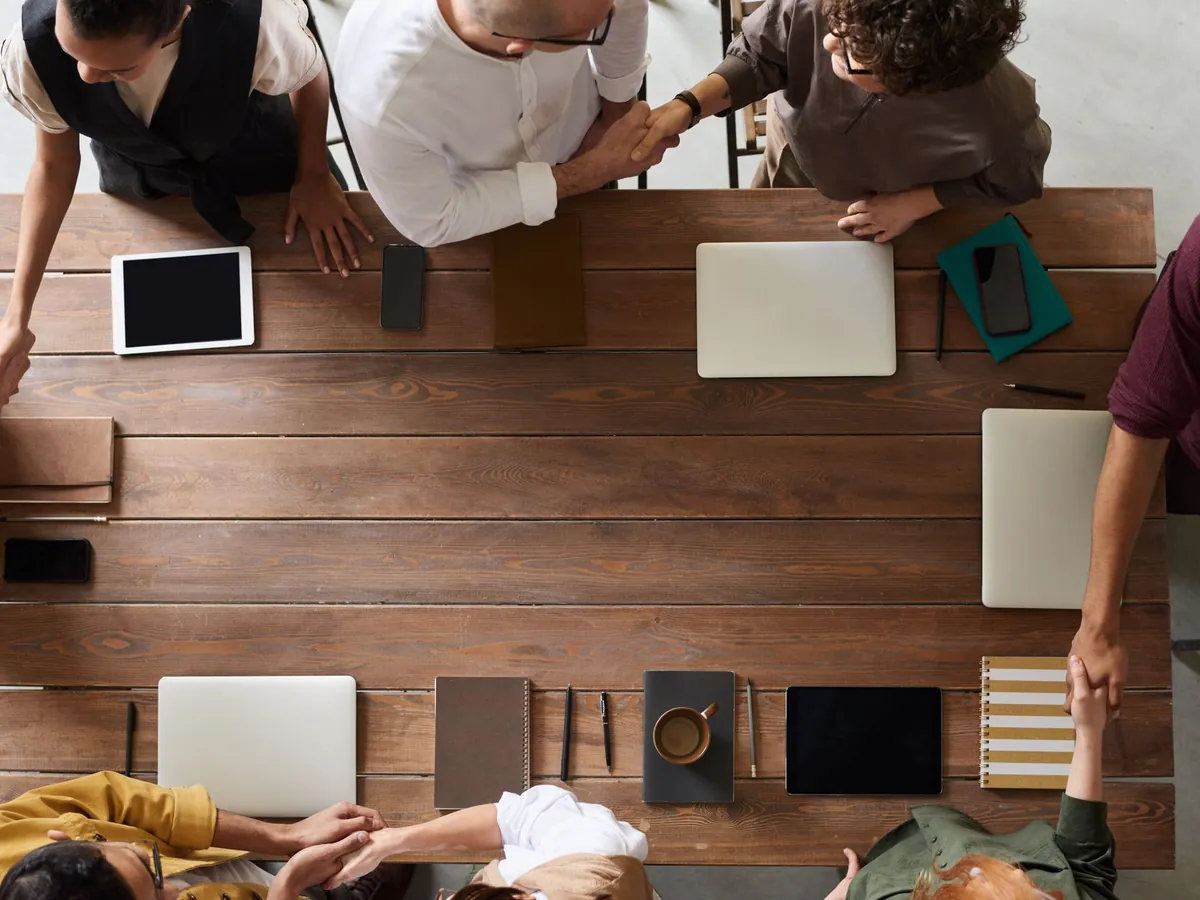 Groupe d'adultes en réunion d'affaires autour d'une table en bois, avec appareils numériques