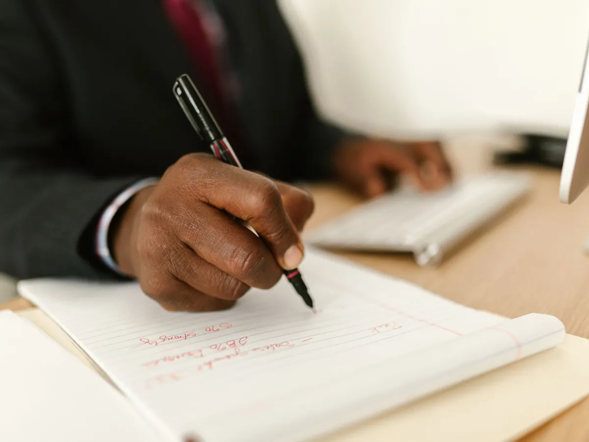 Gros plan d'un homme d'affaires prenant des notes sur un bloc à son bureau, papeterie bien en vue