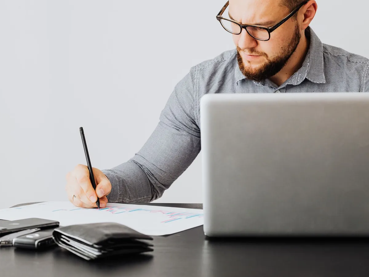 Homme concentré analysant des documents financiers avec son ordinateur portable au bureau