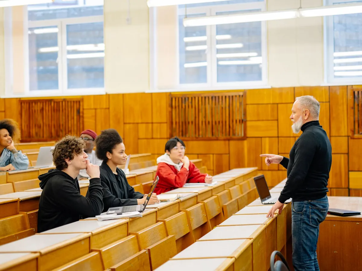 Enseignant échangeant avec des étudiants installés avec leurs ordinateurs dans un amphithéâtre