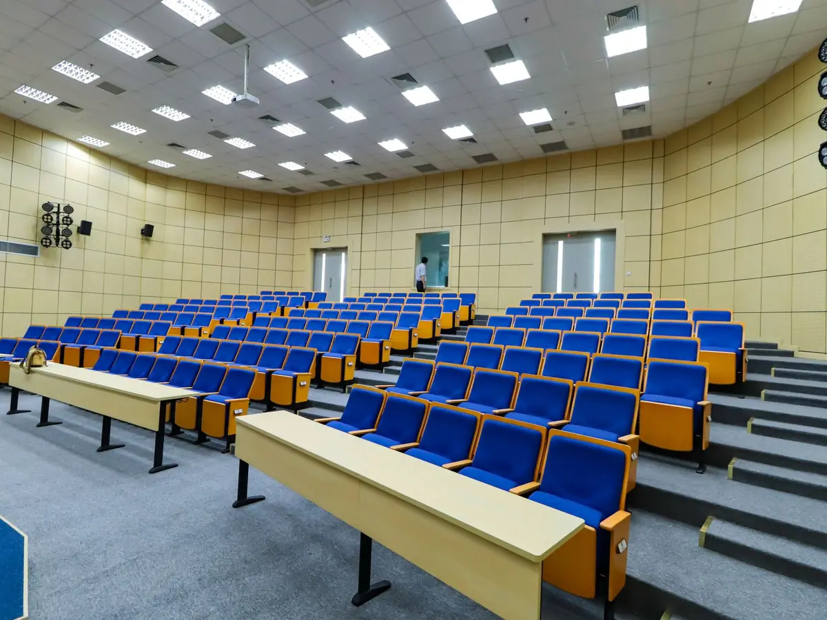 Vaste amphithéâtre aux sièges bleus et aux pupitres, prêt pour accueillir les étudiants