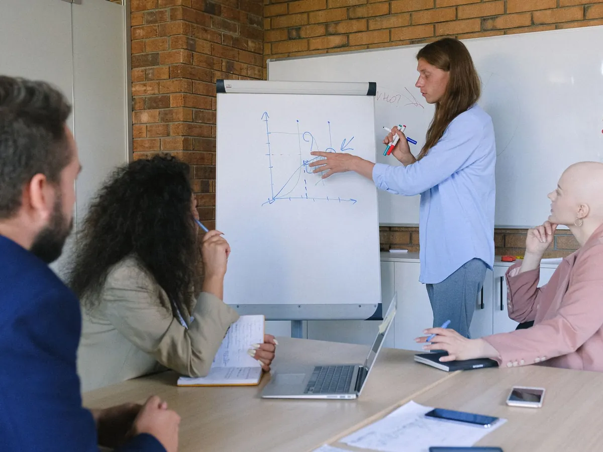 Collègues pensifs à une table en bois, écoutant une présentation de graphique sur tableau de conférence