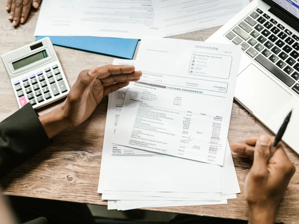 Mains tenant des documents financiers avec calculatrice et ordinateur portable sur un bureau, scène d'analyse