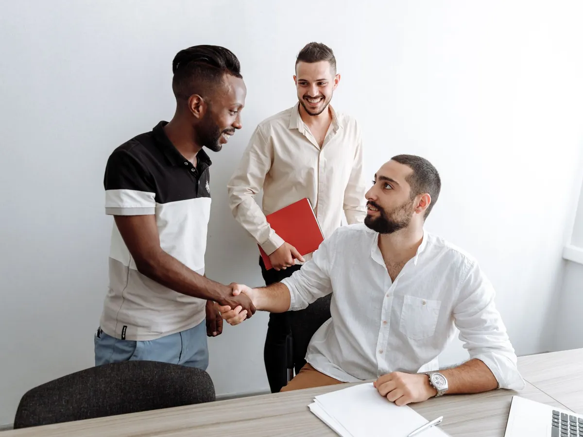 Trois hommes au bureau échangeant une poignée de main amicale, symbole de travail d'équipe