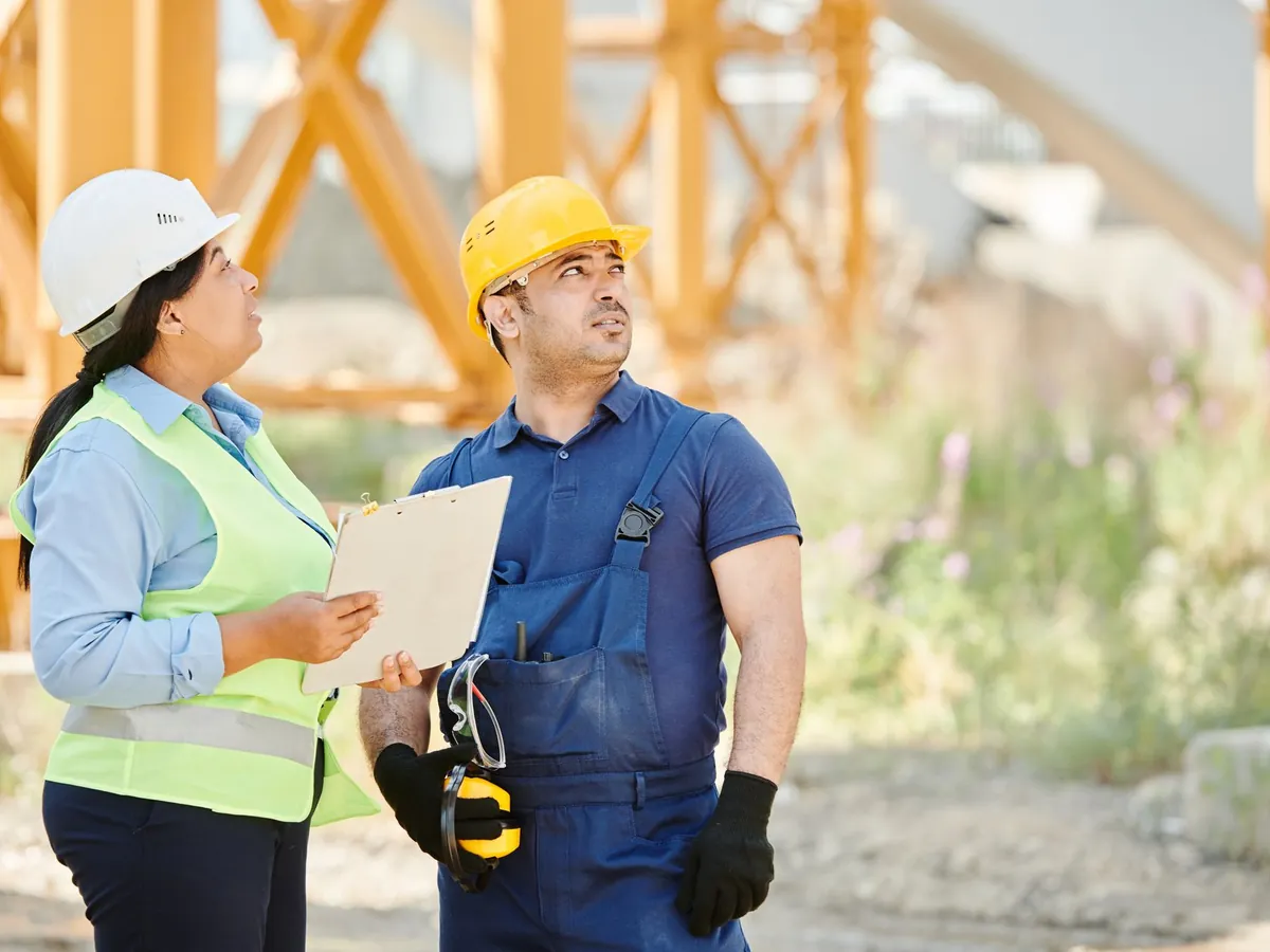 Deux professionnels du bâtiment en casque et gilet consultant un plan sur un chantier