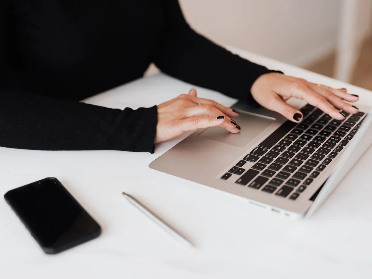 Mains d'une utilisatrice sur le clavier d'un ordinateur portable posé sur un bureau blanc