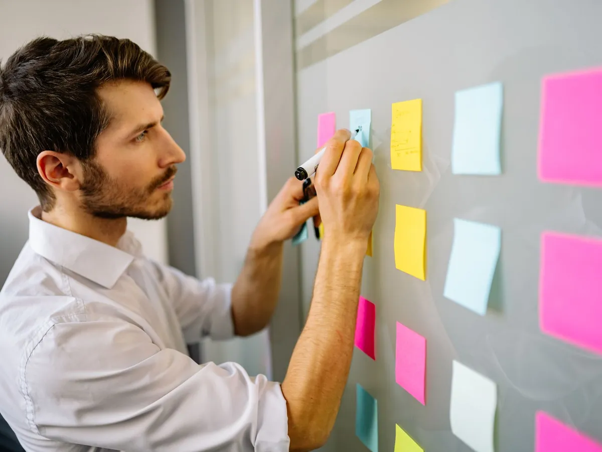Chef de projet organisant des tâches avec des notes adhésives sur un mur vitré