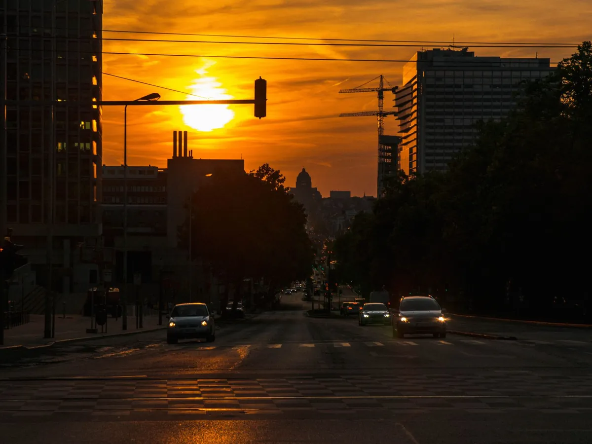 Coucher de soleil sur une rue animée de Bruxelles, bâtiments et véhicules se détachant sur le ciel vif
