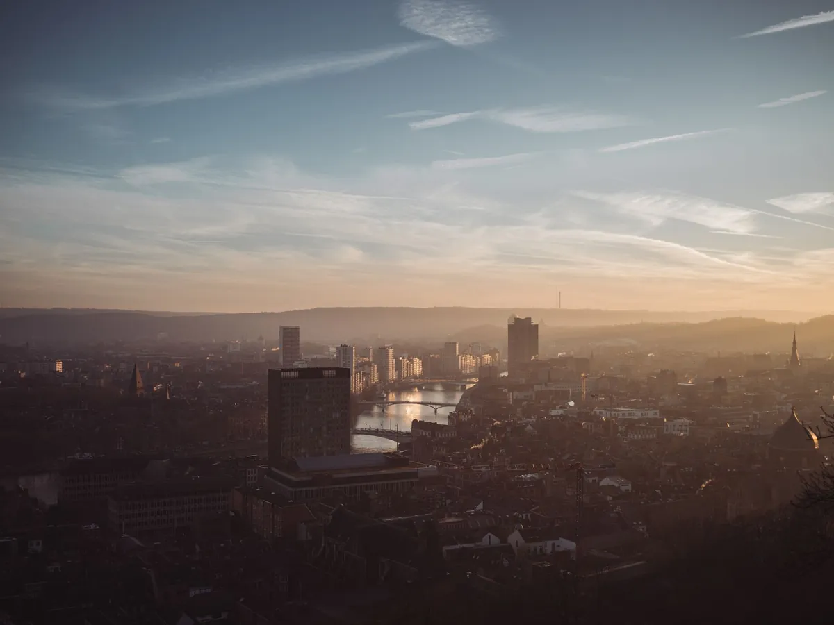 Vue panoramique de Liège aux teintes chaudes du coucher de soleil, reflétée sur la Meuse