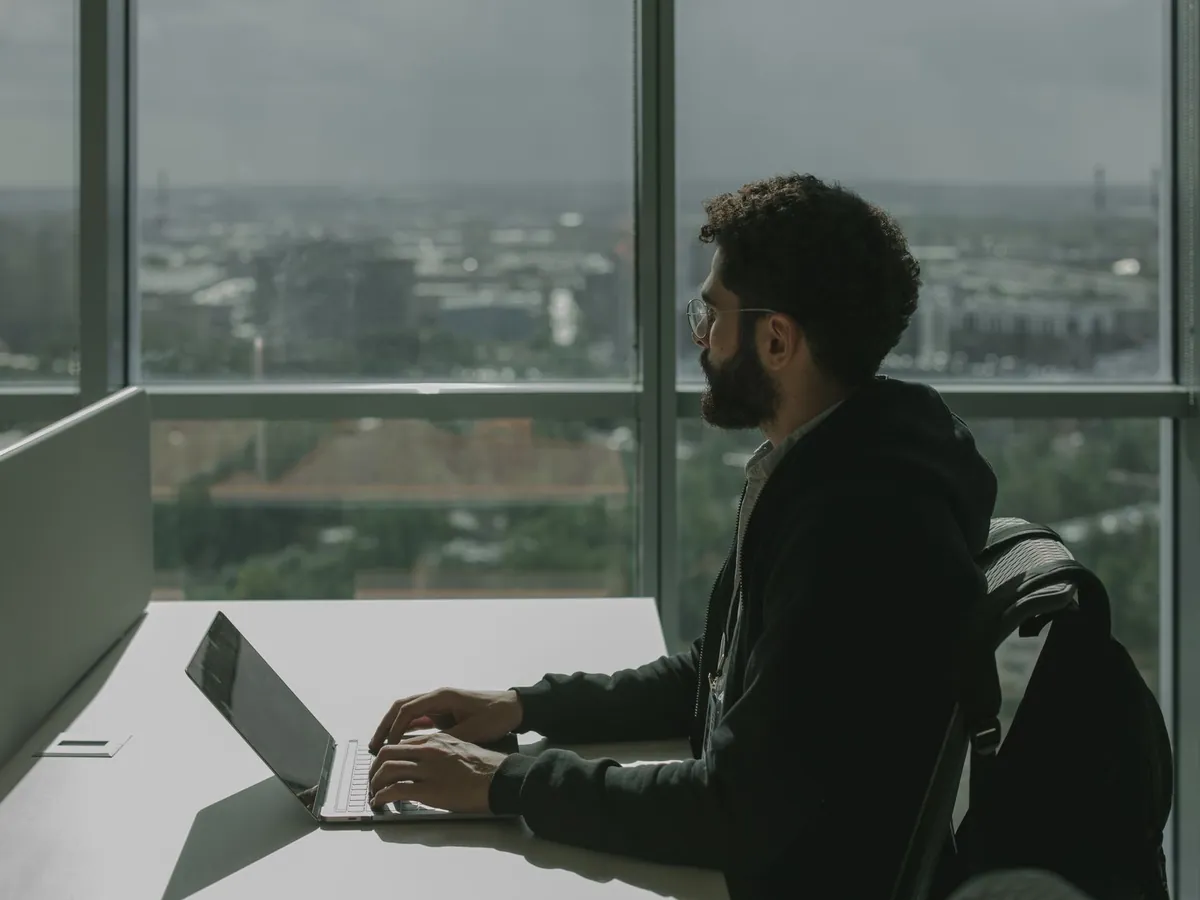Homme barbu tapant sur un ordinateur portable à un bureau moderne avec vue sur la ville