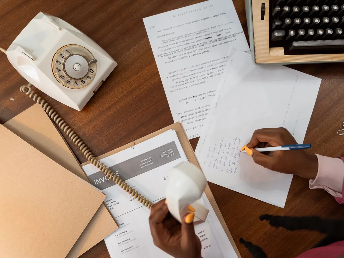 Vue de dessus d'une personne prenant des notes tout en tenant un téléphone vintage sur un bureau en bois